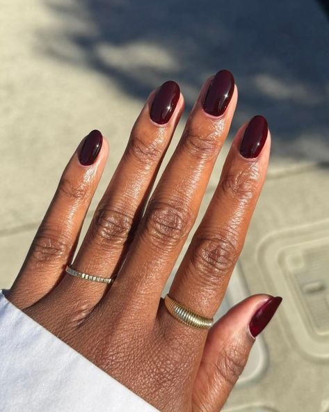 Black cherry short oval nails on dark skin photographed outdoors, sunlight catching the red undertone
