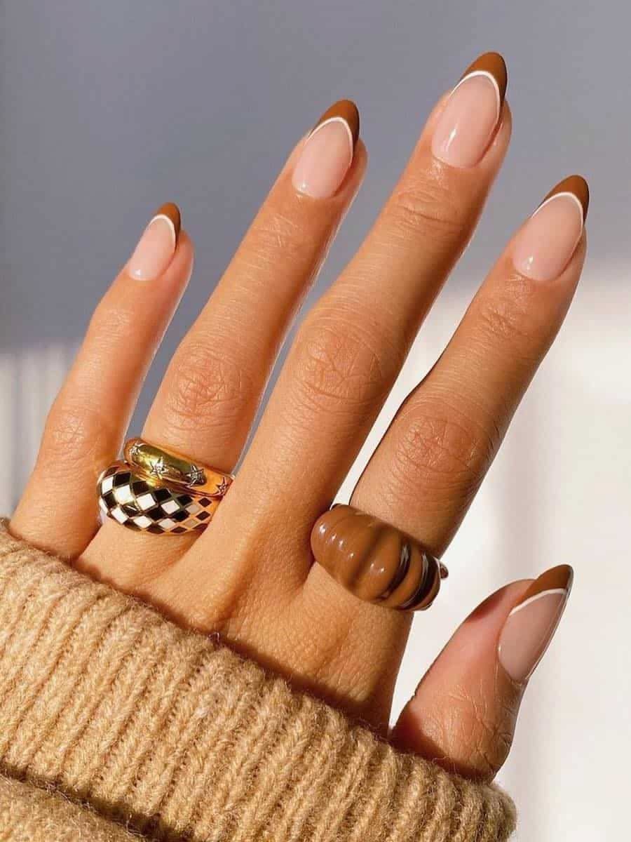 Caramel French tip nails, warm caramel tips on a nude base on a hand in a camel knit sweater with statement rings