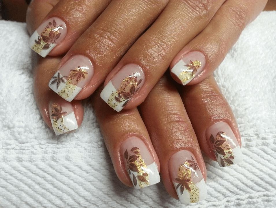 Short square nails with fall leaf art in gold and rust on a milky base, on brown skin over a white towel